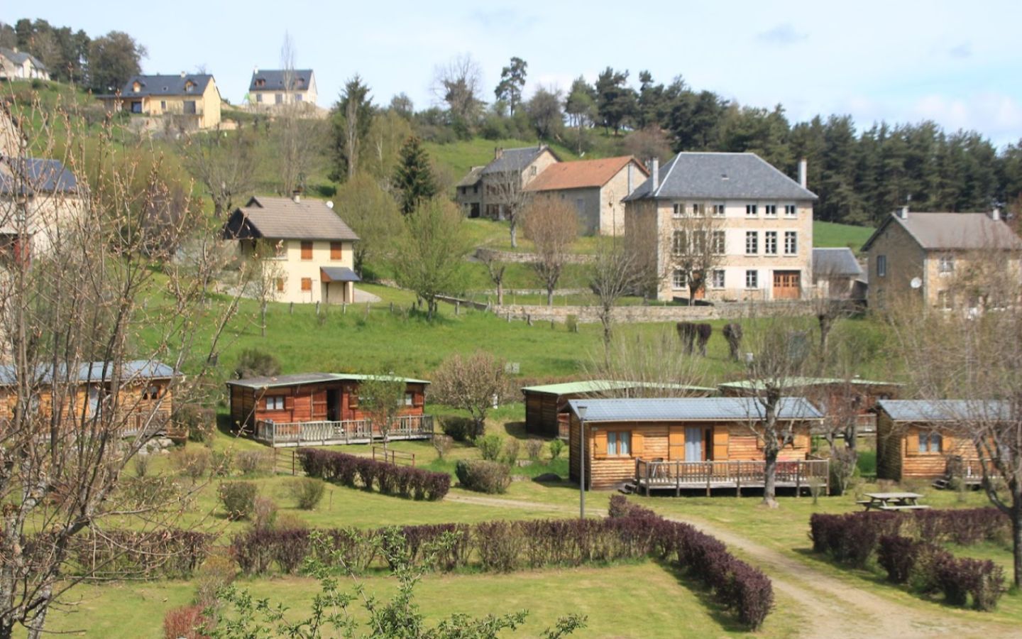 Cette image montre un paysage rural avec plusieurs maisons en bois et en pierre dispersées sur une colline verdoyante. A